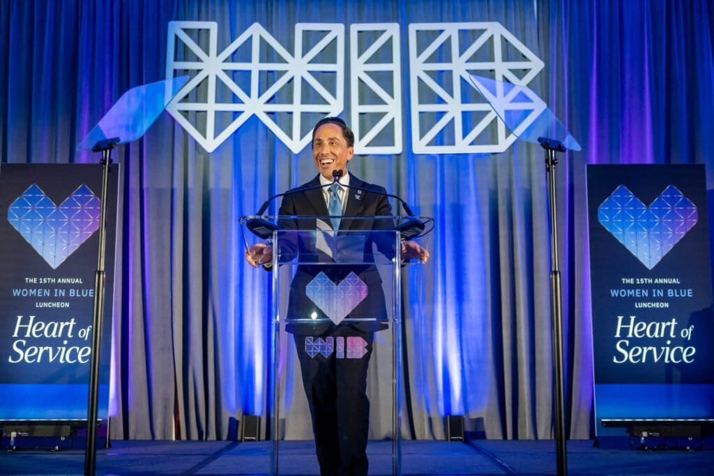 San Diego mayor speaking at the podium during the Women in Blue luncheon, framed by Heart of Service stage graphics.